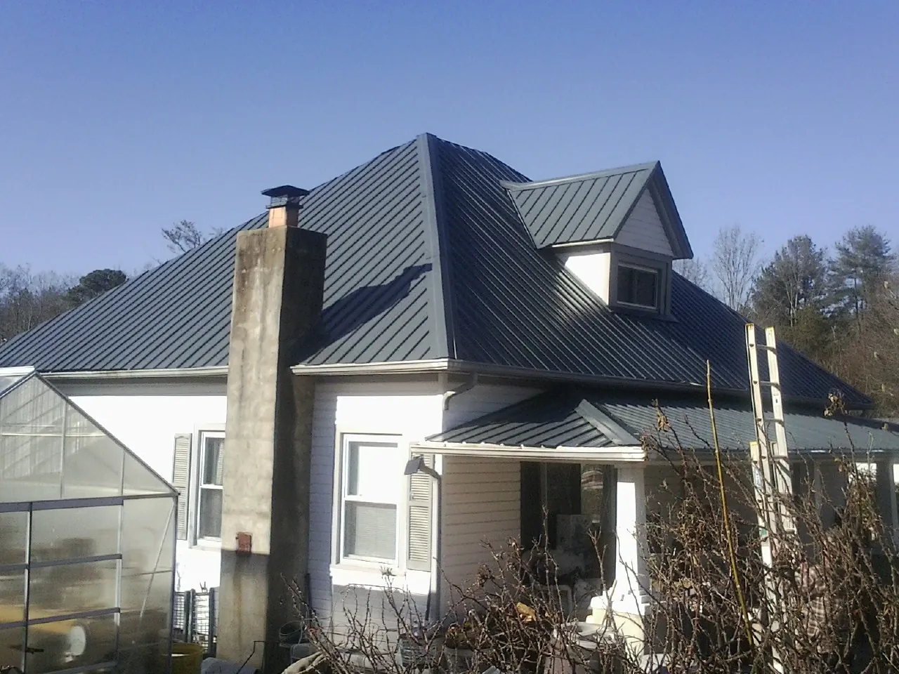Dark blue standing seam metal roof on a white farmhouse with dormer — Slate & Tile Roof Repair by Roofing Brothers in Kidder