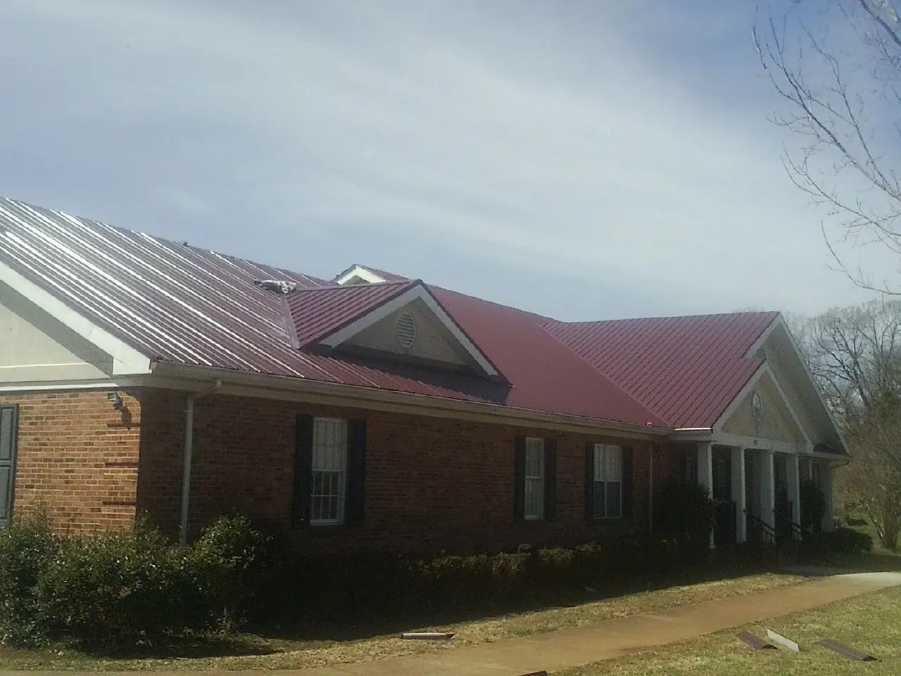 Red metal roof with gabled entries on a long brick building, from a Hail Damage Roof Repair job in Kidder