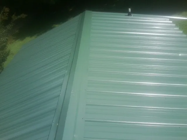New green metal panels meeting at the ridge of a roof — Flat Roof Repair work by our crew in Kidder