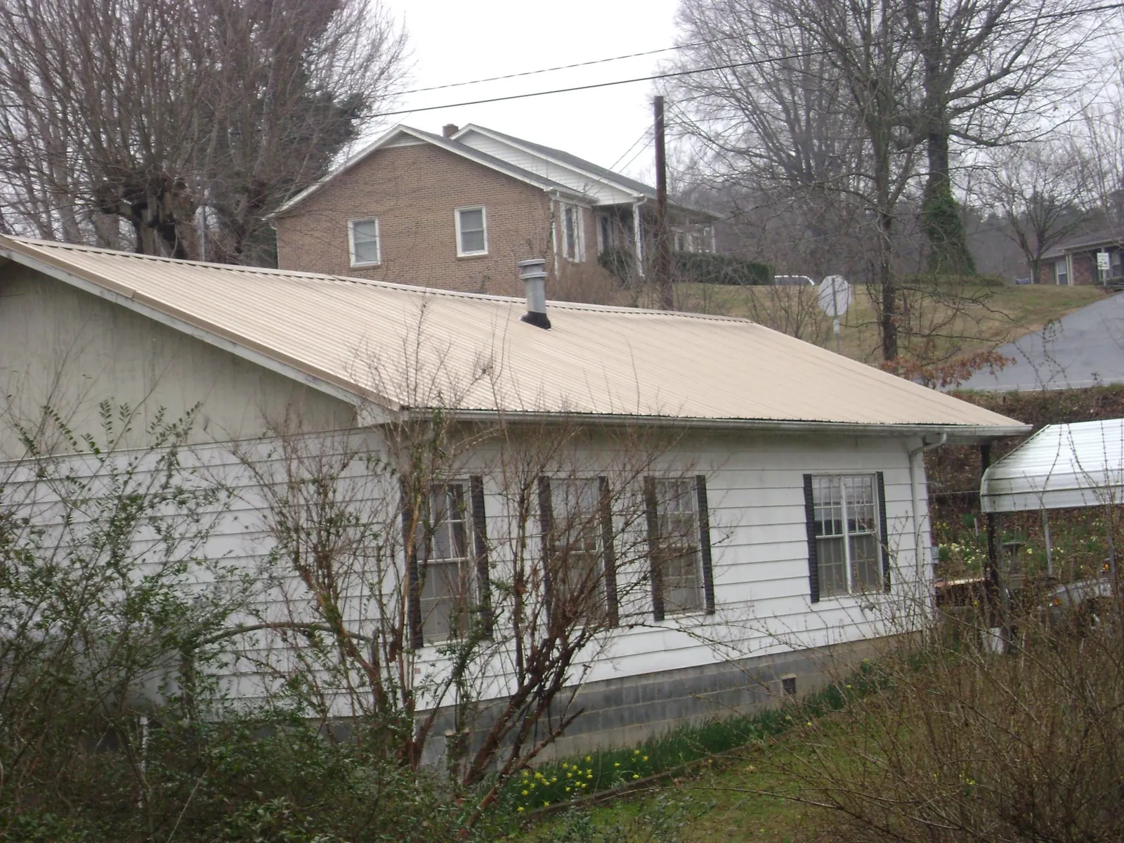 Tan metal roof on a white sided house set into a hillside — Commercial Roofing by Roofing Brothers in Kidder